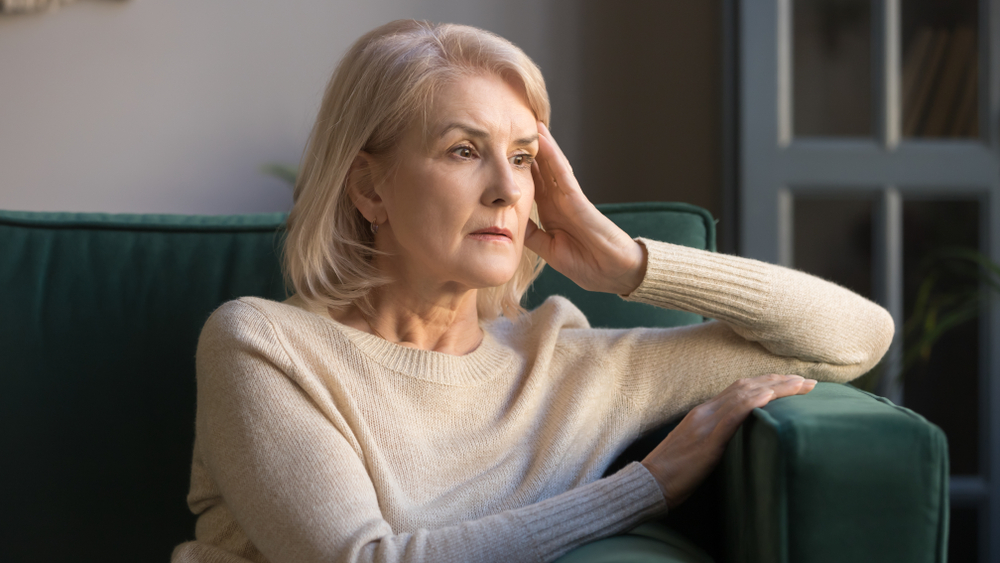 Older woman looking anxious, sitting on a sofa resting her head on her hand