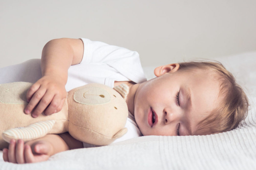 baby holding a teddy bear sleeping peacefully on a bed