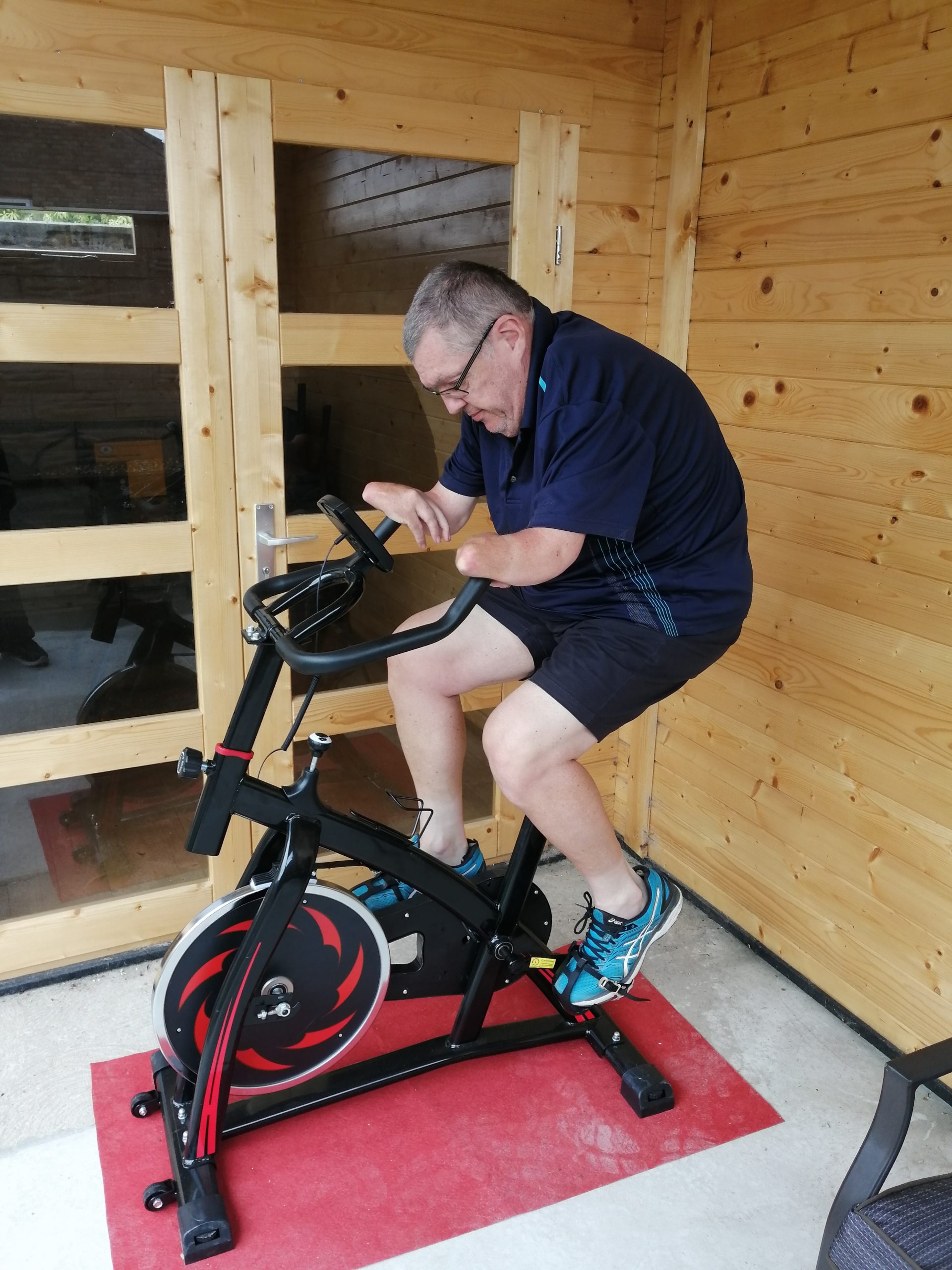 Neal Merry on his exercise bike which has handle bars pointing back towards the seat with upward angled ends his to suit his arms
