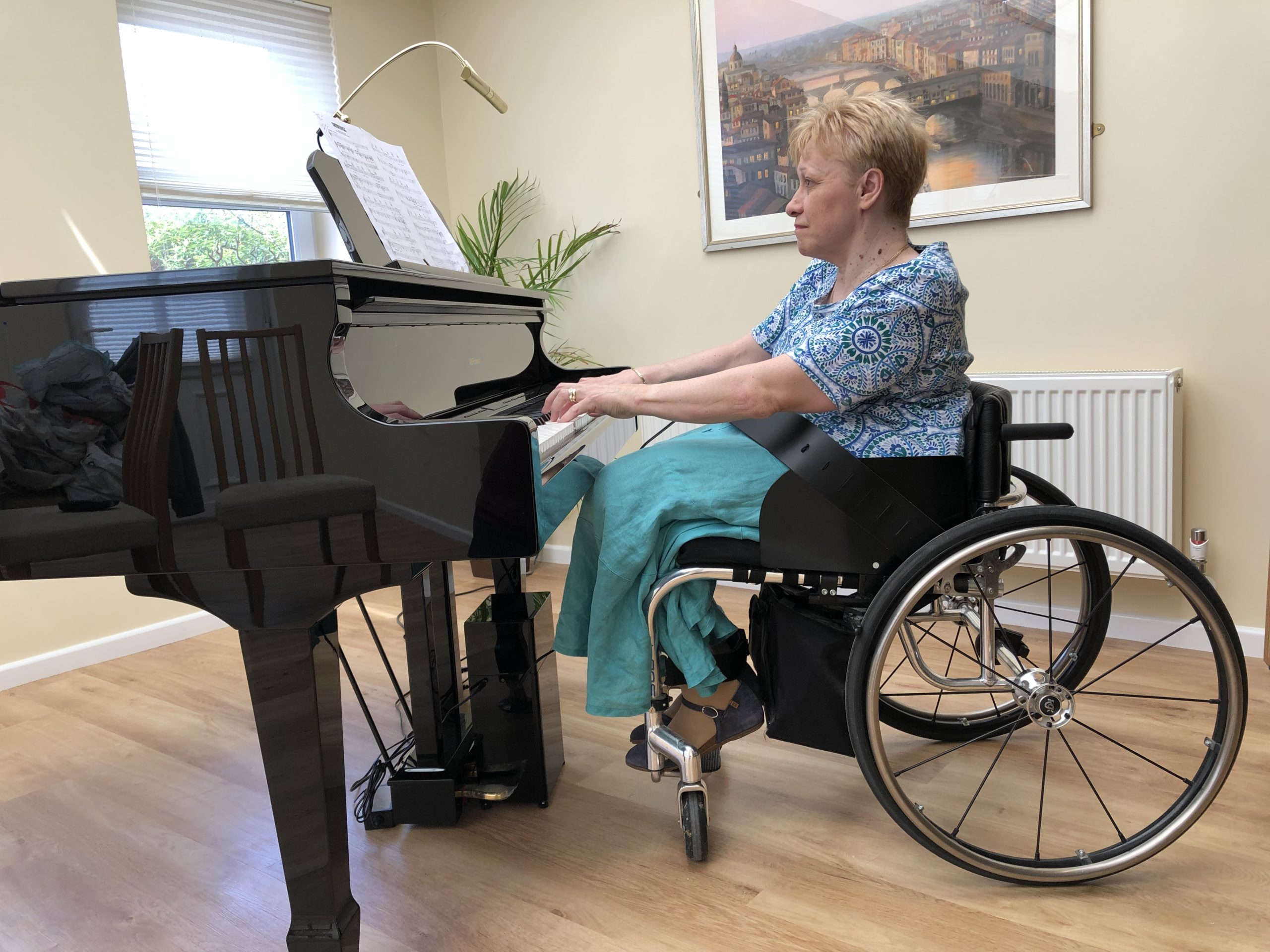 Sally Stevens sitting at her grand piano in her wheelchair playing a piece of music