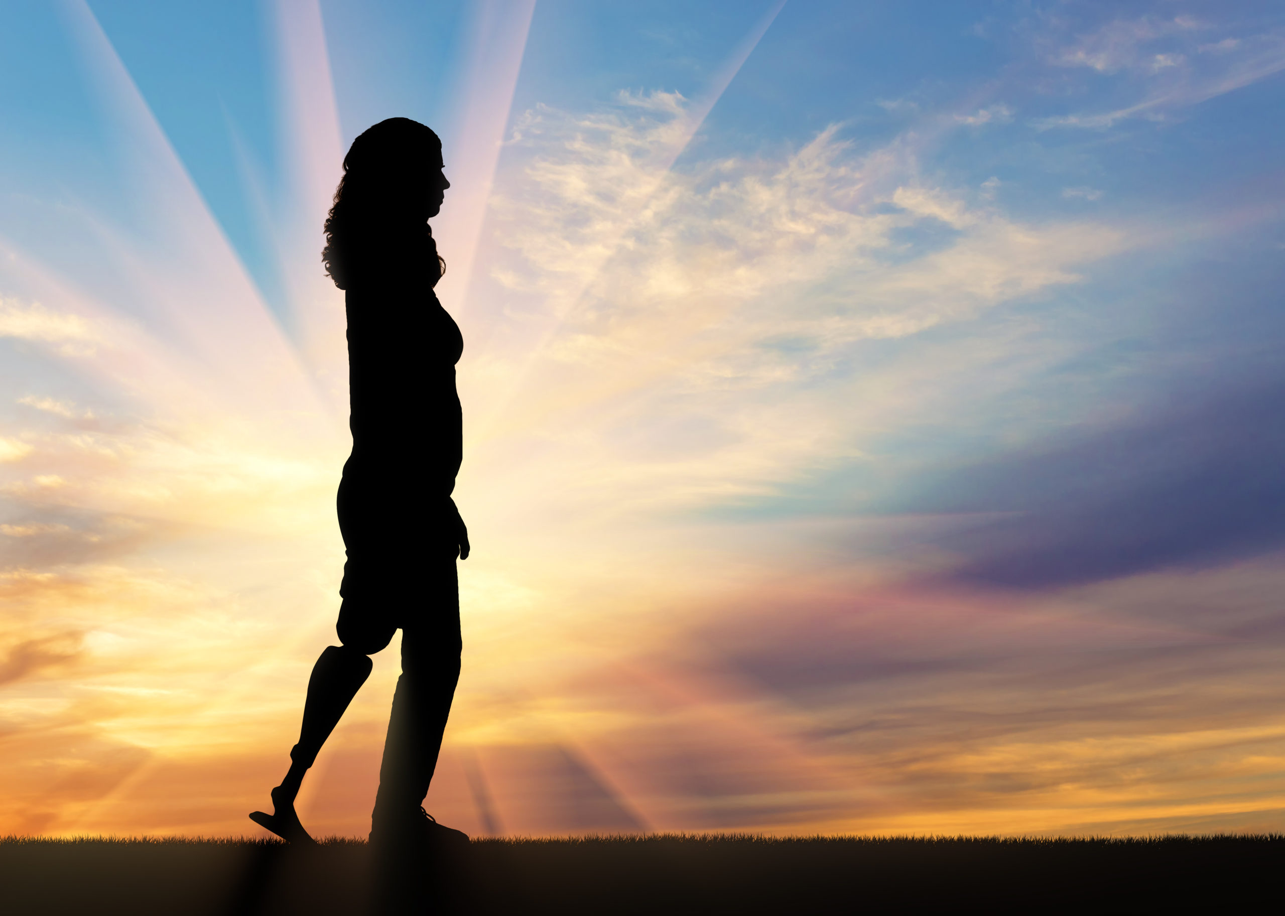 Woman in silhouette walking with a prosthetic leg against a sunset sky