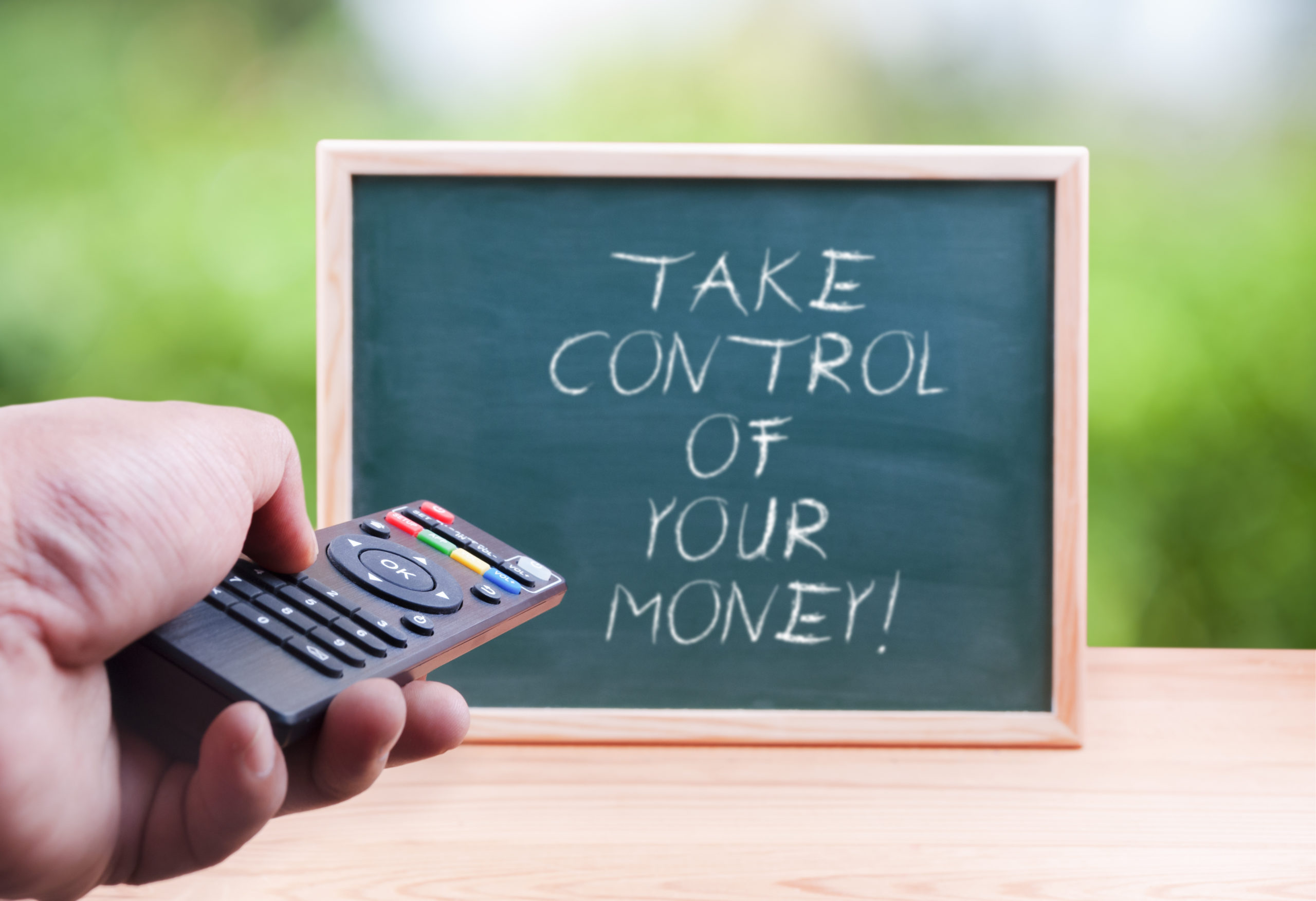 Hand holding a remote control device pointing at a blackboard with the words Take control of your money' on it
