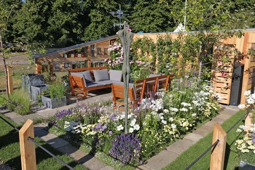 garden with borders and pots arranged in parallel or perpendicular lines, the borders heavily feature daisies, the dominant colours are white and purple, there is also a seating area for relaxing