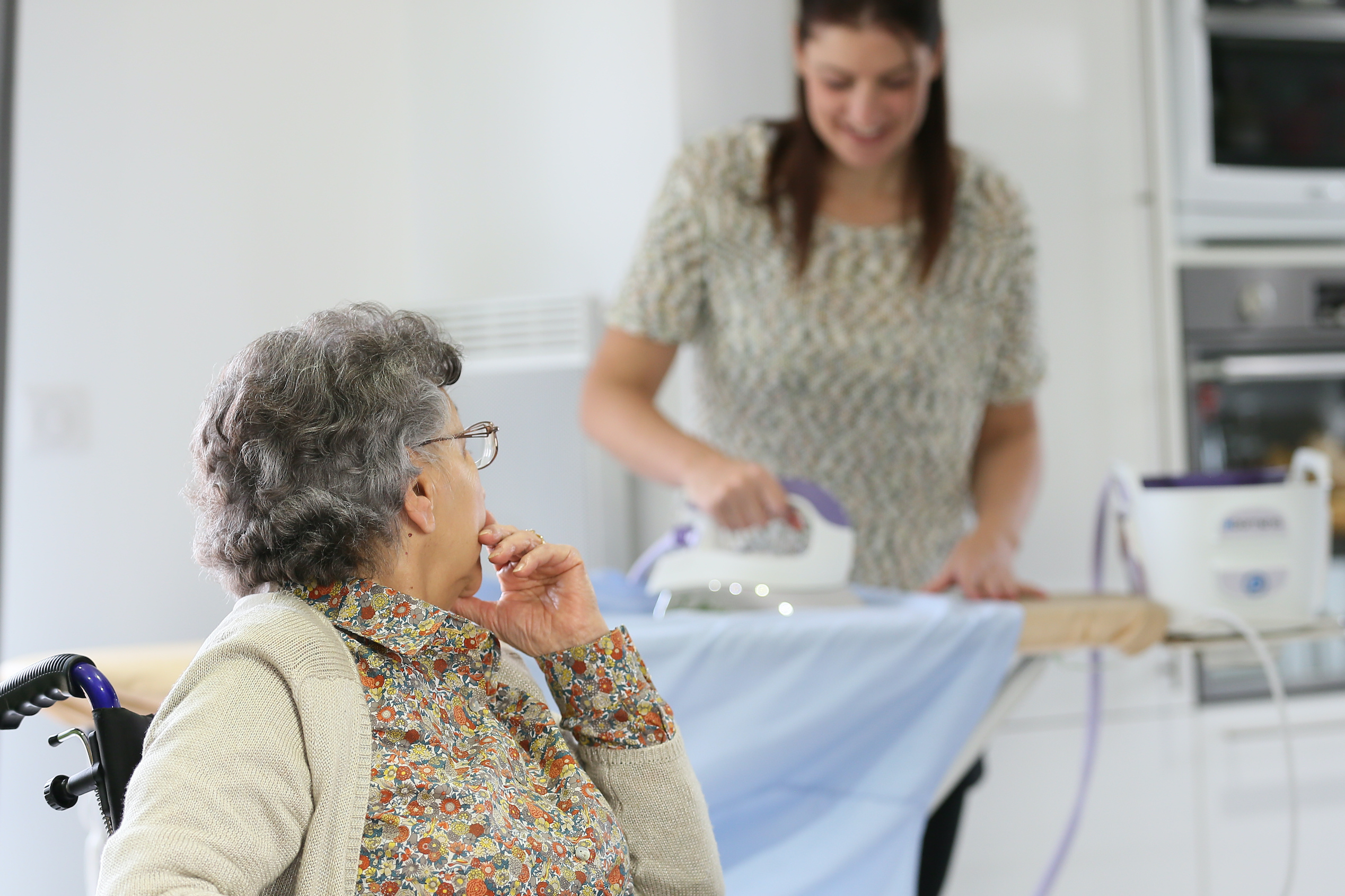 private carer ironing clothes for elderly client in wheelchair