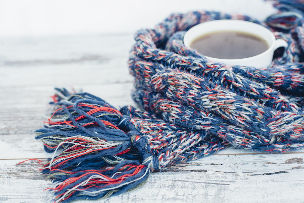 Cup of black tea on wooden table wrapped in warm woven scarf