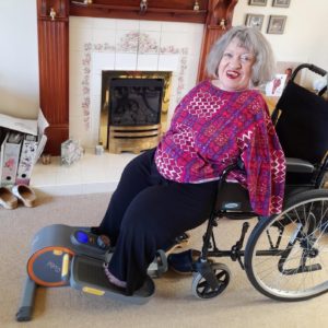 Morag perched on the edge of her wheelchair seat with her feet on large pedals of a static leg exercise machine