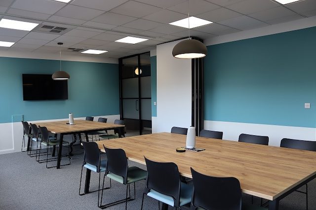 Large room with 2 large tables with chairs a TV on the back wall and a fold-away dividing wall which can be used as flexible office space
